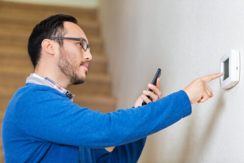 Homeowner adjusting thermostat with smartphone